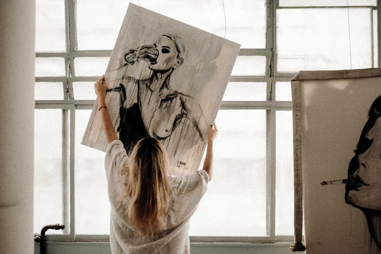 fernanda romão segurando uma pintura junto à janela do ateliê